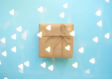 Hediye kutusu kahverengi renkli Kraft kağıt sarılı ve tope kalp şeklinin ışıkları ile mavi arka plan ile bağlı.