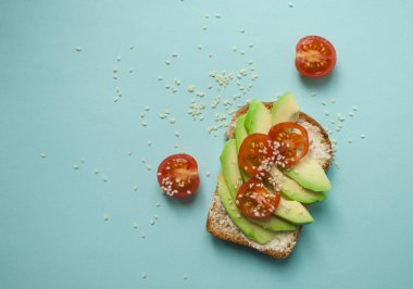 Düz lezzetli tost dilimlenmiş avokado, domates ve sesamum tohum boşaltmak mavi zemin üzerine yatırın. Sağlıklı gıda kavramı.