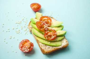 Düz lezzetli tost dilimlenmiş avokado, domates ve sesamum tohum boşaltmak mavi zemin üzerine yatırın. Sağlıklı gıda kavramı.