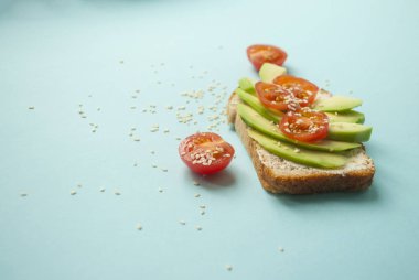 Düz lezzetli tost dilimlenmiş avokado, domates ve sesamum tohum boşaltmak mavi zemin üzerine yatırın. Sağlıklı gıda kavramı.