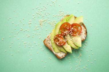 Düz lezzetli tost dilimlenmiş avokado, domates ve sesamum tohum boşaltmak turqouise zemin üzerine yatırın. Sağlıklı gıda kavramı.