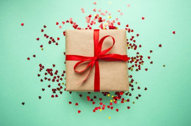 Hediye kutusu kahverengi renkli Kraft kağıt sarılı ve kırmızı konfeti ile mavi arka plan üzerinde kırmızı yay ile bağlı.