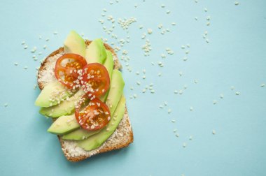 Düz lezzetli tost dilimlenmiş avokado, domates ve sesamum tohum boşaltmak mavi zemin üzerine yatırın. Sağlıklı gıda kavramı.