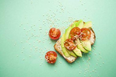 Düz lezzetli tost dilimlenmiş avokado, domates ve sesamum tohum boşaltmak turkuaz zemin üzerine yatırın. Sağlıklı gıda kavramı.