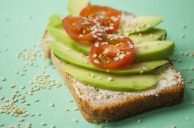 Lezzetli tost dilimlenmiş avokado, domates ve sesamum tohumlar üzerinde boşaltmak ile mavi arka plan ile. Sağlıklı gıda kavramı.