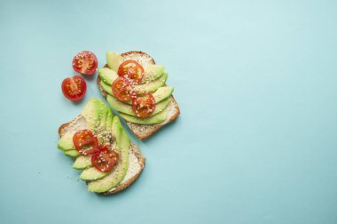Düz lezzetli tost dilimlenmiş avokado, domates ve sesamum tohum boşaltmak mavi zemin üzerine yatırın. Sağlıklı gıda kavramı.