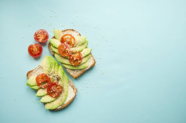 Düz lezzetli tost dilimlenmiş avokado, domates ve sesamum tohum boşaltmak mavi zemin üzerine yatırın. Sağlıklı gıda kavramı.