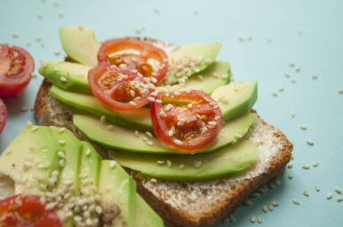 Dilimlenmiş avokado, domates ve sesamum tohumlar boşaltmak ile mavi arka plan üzerinde bir sandviçle, yakın çekim.