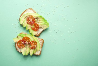 Düz lezzetli tost dilimlenmiş avokado, domates ve sesamum tohum boşaltmak mavi zemin üzerine yatırın.