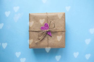Hediye kutusu pembe ışıltılı kalp ile kahverengi renkli Kraft kağıt sarılı ve ip üzerinde mavi arka plan ile bağlı.