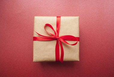 Hediye kutusu pastel pembe bir arka plan üzerinde kırmızı kurdele ile bağlanmış.