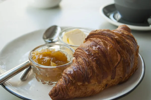 Croissant with jam, butter and a cup of coffee. — Stock Photo, Image