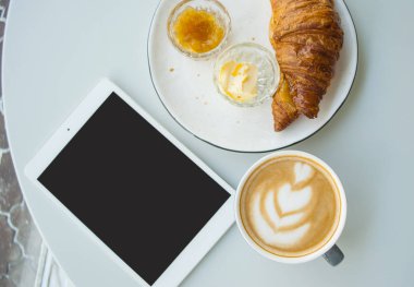 Taze kruvasan reçel, tereyağı ve kapuçino güzel latte sanat bir kafede gri tablosundaki ile. Sabah rutin.