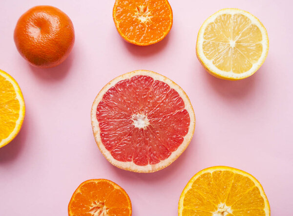 Flat lay of cut ripe juicy grapefruit, lemon and orange on pink background. Citrus pattern.
