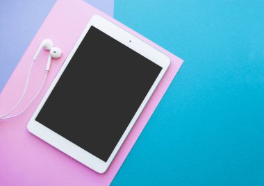 Düz beyaz tablet ve mavi, mor ve pembe arka plan üzerinde kulaklık ile boşaltmak yatıyordu.