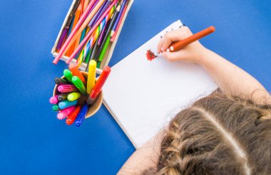 Çocuğun çizimleri renkli kalemler ve işaretleyicilerle mavi arkaplandaki bir defterde kopyalanmış. Düz yatış stili. Okul konseptine dönelim..