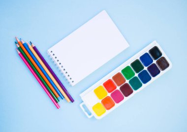 Renkli kalemler, defter, boya fırçası ve mavi arka planda telif alanı olan suluboya boyalar. Düz yatış stili. Okul konseptine dönelim..