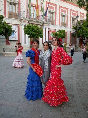 Seville İspanya/16 Nisan 2013 / iki genç İspanyol bayanlar içinde parlak icoloured geleneği elbise poz ile bir turist yıllık Nisan bahar Fuarı'nda düzenlenen Sevilla şehir İspanya '