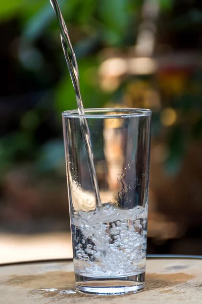 Beba água derramando em vidro e fundo verde natural — Fotografia de Stock