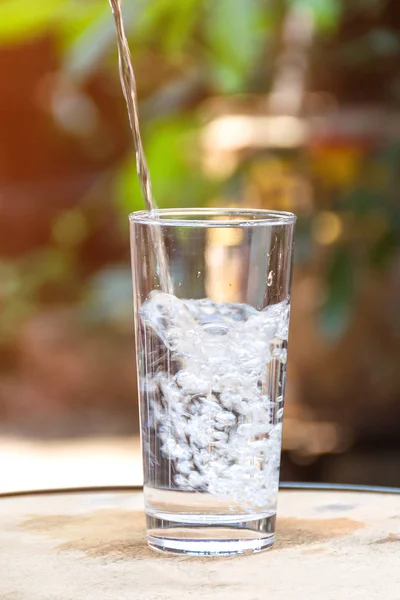 Beba água derramando em vidro e fundo verde natural — Fotografia de Stock