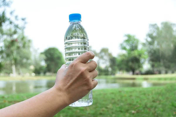 Mão segurando garrafa de água potável no fundo da natureza — Fotografia de Stock