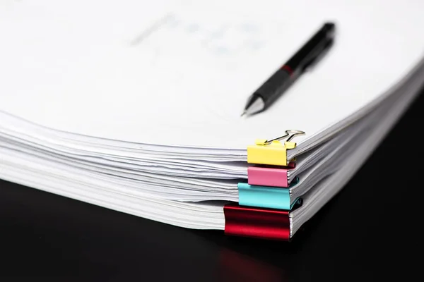 Pile or Stack of documents with colorful clips on black background.