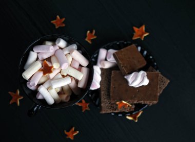 Sütlü çikolata ve şekerleme ahşap arka plan üzerinde ile siyah plaka ve bir fincan kahve pembe Marshmallow