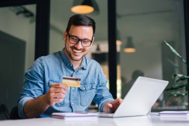 Mutlu, güler yüzlü, yetişkin bir adam online alışveriş yapıyor ya da internet üzerinden ödeme yapan girişimci ya da serbest çalışan serbest çalışan işçi ücreti topluyor.