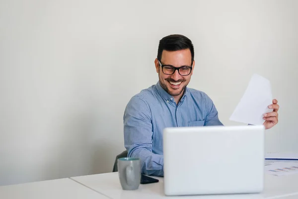 Молодой улыбающийся веселый бизнесмен в офисе работает с ноутбуком — стоковое фото