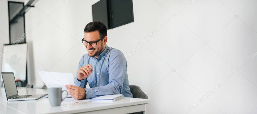 Young smiling cheerful confident businessman checking working plan and schedule or timetable in office copy space