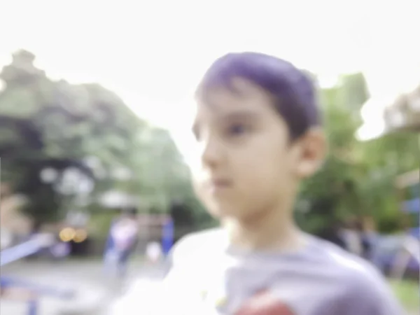 Blurred portrait close up shot of boy child in urban city park playground looking out of frame blur out of focus image young children going to play with friends background backdrop