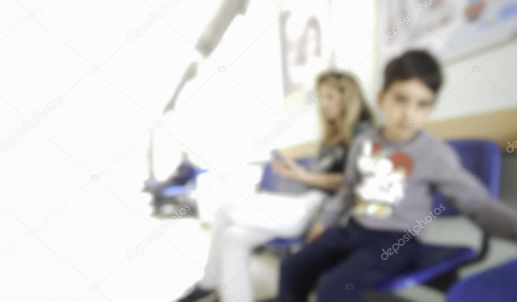 Blurred image of mother and young son child in a waiting room at hospital clinic sitting and waiting to see doctor for check up or other medical staff clipping white copy space looking at camera