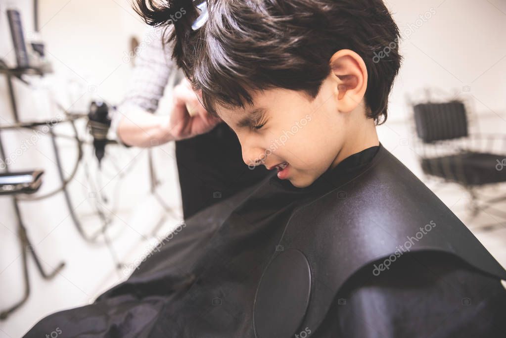 I don't like hair cut it hurts me little young child boy toddler at barbershop hairdresser saloon protesting against hair cut in pain and hurt scared painful experience first time hair cut close up