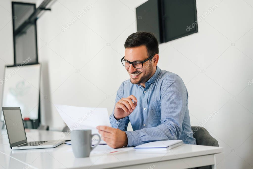 Young smiling cheerful confident businessman checking working plan and schedule or timetable in office copy space screen empty modern bright