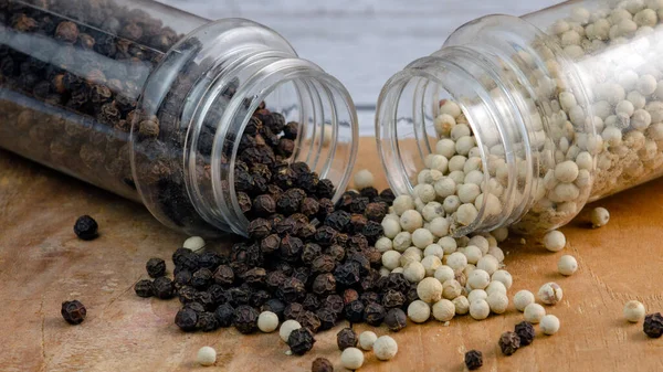 Plastik mutfak çeşnili beyaz / siyah biber ahşap zemin üzerine saçılmıştır.