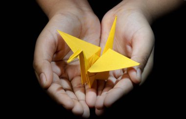 El ele tutuşan Origami Kağıt Turna (Orizuru), Siyah Arkaplanda Sarı Kuş 