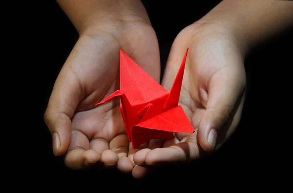 El ele tutuşan Origami Kağıt Turna (Orizuru), Kırmızı Kuş. Siyah Arkaplan 
