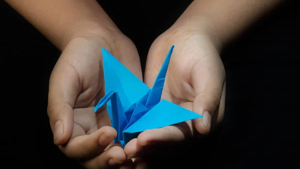 El ele tutuşan Origami Kağıt Turna (Orizuru), Mavi Kuş. Siyah Arkaplan 