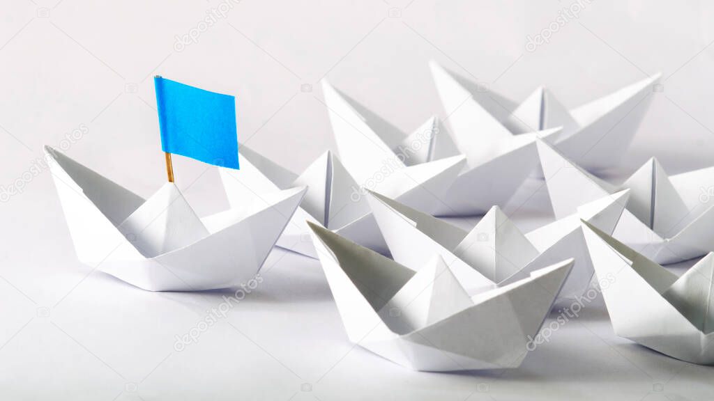 Leadership concept. Blue flag Origami White Paper boat (ship) leading the others.  One leader ship leads other ships.