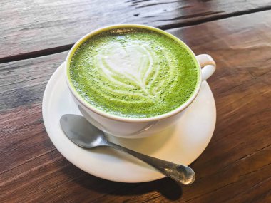 Sıcak matcha yeşil çay süt latte kremsi süt ile kalp şeklinde desen, ahşap masada bir fincan biraz şeker ve çay kaşığı.