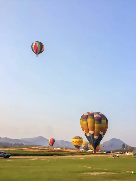 Colorful hot air balloon floating over meadow with mountain and blue sky at Singha Park Chiang Rai International Balloon Fiesta.