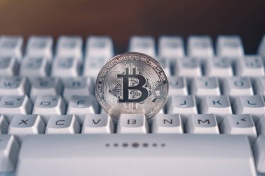 Turuncu ışıklı beyaz bir klavyede gümüş bitcoin. Şifreli sanal para. Engelleme teknolojisi kavramı.