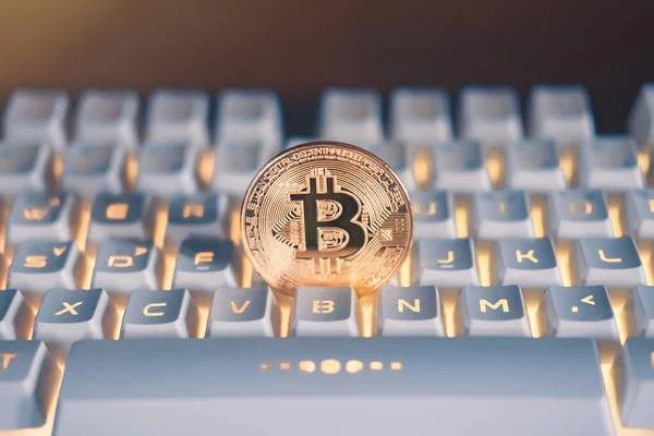 Sarı ışık ya da RGB klavyesi ve turuncu ışık fişeği olan beyaz bir klavyede altın bitcoin. Şifreli sanal para. Engelleme teknolojisi kavramı.