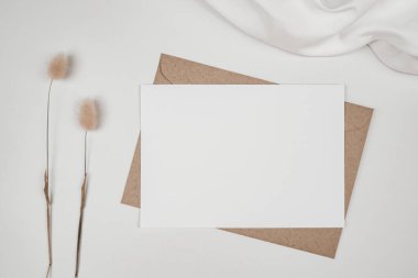 Kahverengi kağıt zarfın üzerine boş beyaz kağıt. Tavşan kuyruğu, kuru çiçek ve beyaz bez. Yatay boş tebrik kartının bir kopyası. Beyaz arkaplandaki el işi zarfının üst görüntüsü. Düz minimalizm yatıyordu