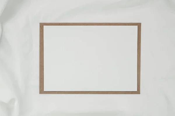 Blank white paper on brown paper envelope with white cloth. Mock-up of horizontal blank greeting card. Top view of Craft envelope on white background. Flat lay minimalism