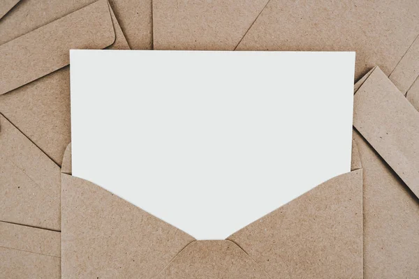 Blank white paper is placed on the open brown paper envelope. Mock-up of horizontal blank greeting card. Top view of Craft paper envelope on white background. Flat lay of stationery. Minimalism style.