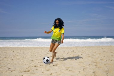 Genç kadın futbol topu kumsalda oynarken