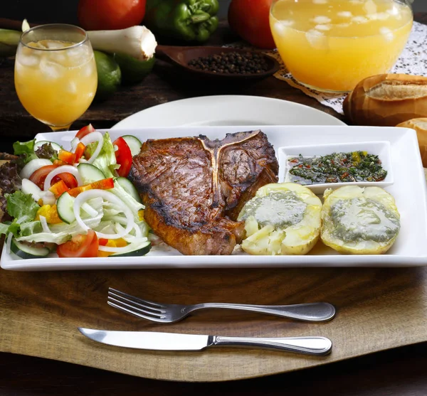 T bone steak with trimmings, potato, salad, orange juice, bread — Stock Photo, Image