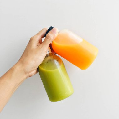 Beyaz bir arka plan üzerinde izole sağlıklı ve taze avokado ve portakal suyu şişeleri tutan el