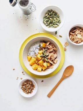 Sağlıklı kahvaltı kaseyle chia tohum puding, mango, tahıl, kabak çekirdeği ve Ayçiçeği tohumları üzerinde bir mutfak masa, beyaz arka plan Üstten Görünüm